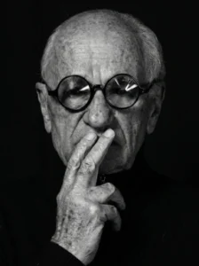 Primer plano en blanco y negro de un hombre mayor con gafas redondas y expresión reflexiva.
