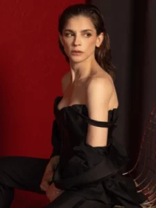 Retrato de perfil de una mujer con vestido negro de hombros descubiertos sobre fondo rojo.